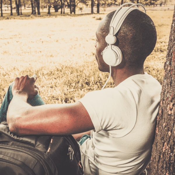 Black Guy Sitting Against A Tree And Listening To Music On Headphones