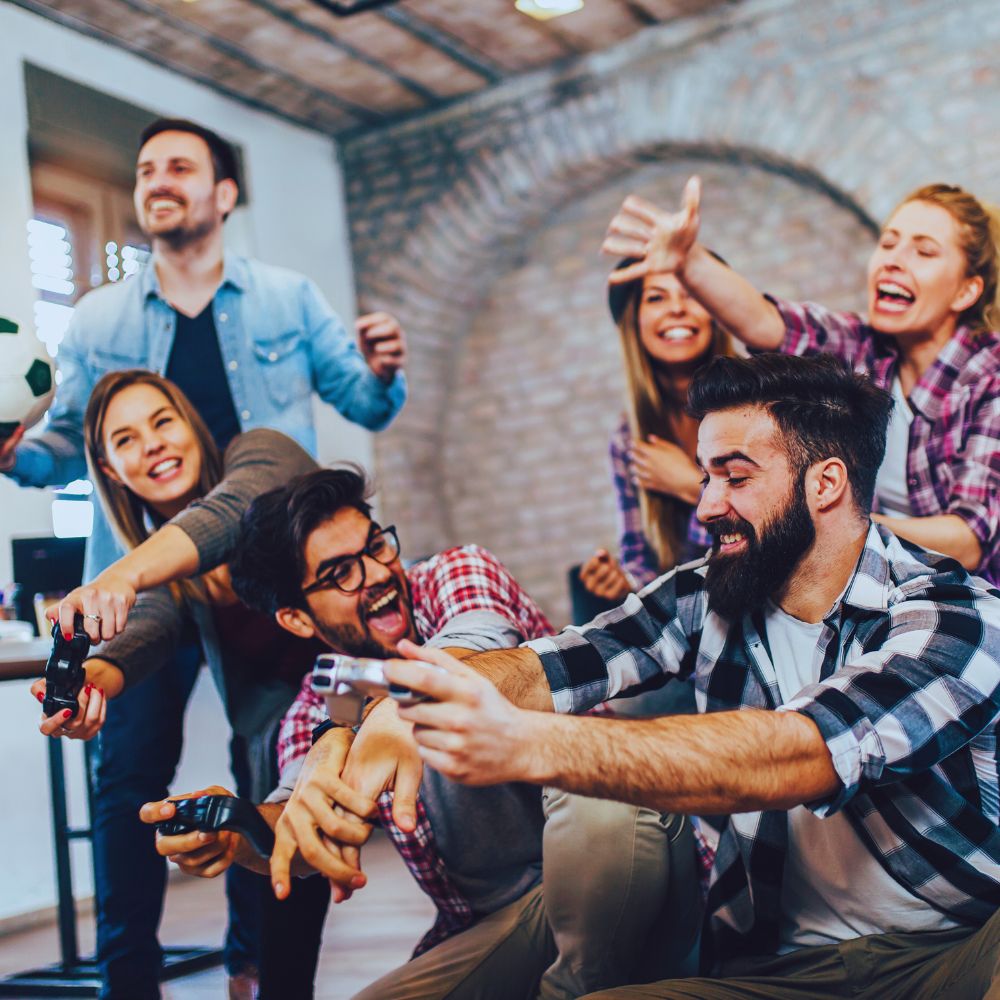 A group of young adults holding console controllers and reacting in a very animated way. In the background a guy is holding a football for some reason